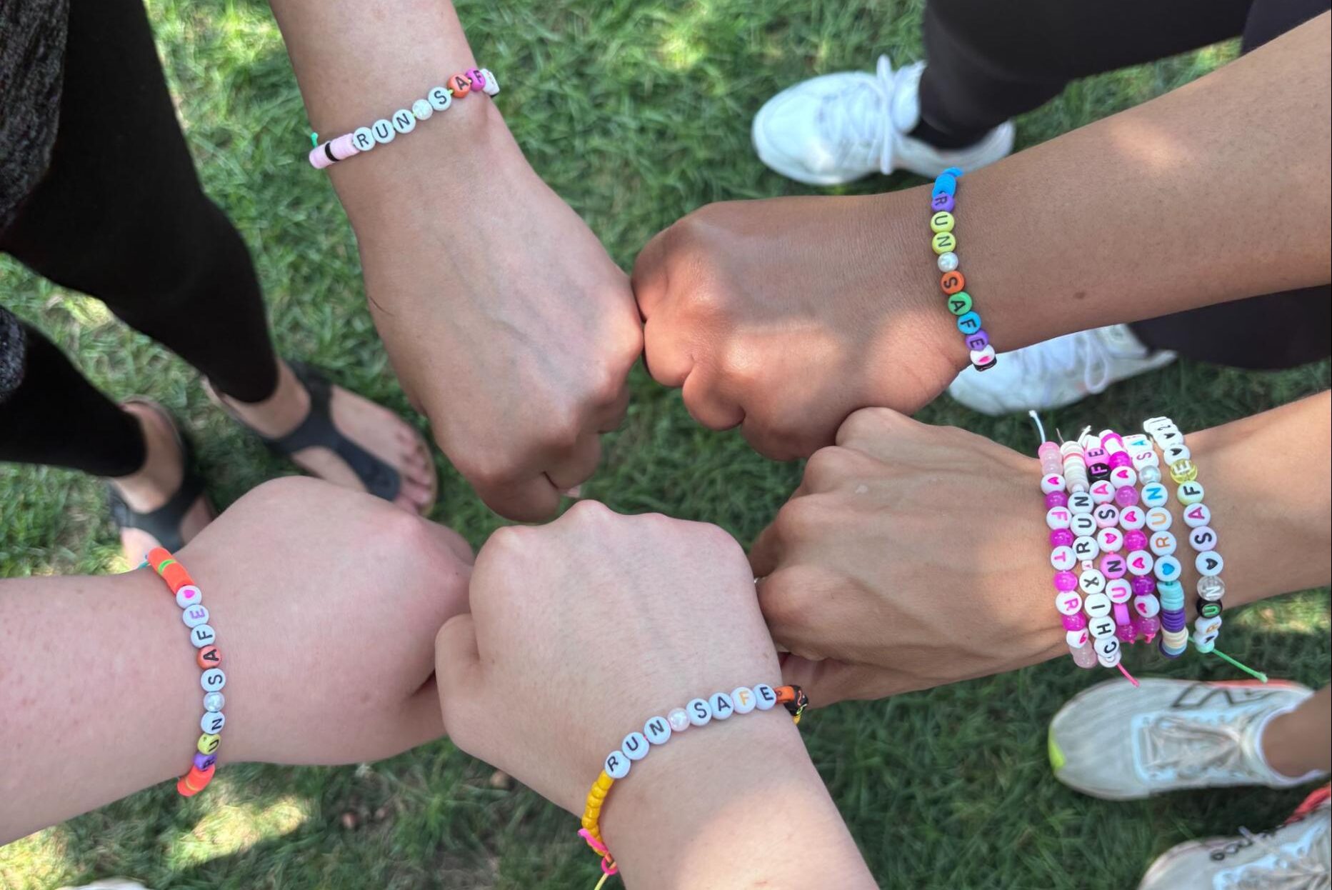 hands placed together over grass wearing beaded bracelets that say 